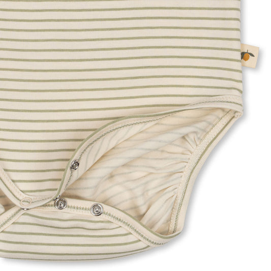 Close-up of a Konges Sløjd long-sleeve bodysuit in soft striped fabric, showing snap button closures at the bottom for easy changing. A small fabric tag with a citrus fruit illustration is visible on the side seam.