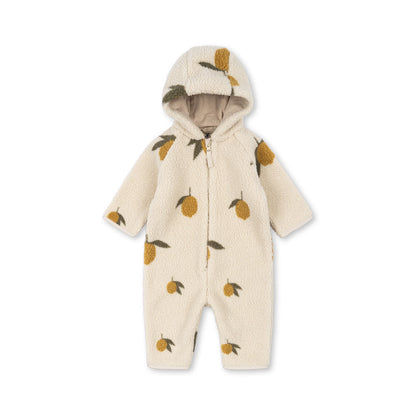 A Konges Sløjd Jody Teddy Onesie in Mon Grand Citron print. This cosy cream-coloured fleece onesie features an all-over lemon pattern with golden-yellow fruit and green leaves. Designed with a zip-up front, a soft-lined hood, and long sleeves, it provides warmth and comfort for little ones during chilly days.