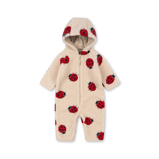 A Konges Sløjd Jody Teddy Onesie in a Ladybird print. This cosy cream-coloured fleece onesie features an all-over pattern of red and black ladybirds. Designed with a zip-up front, a soft-lined hood, and long sleeves, it provides warmth and comfort for little ones, making it a playful and snug choice for colder days.