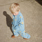 A toddler in the Konges Sløjd Lemon Denim set walking outdoors in the sunlight. The jacket’s relaxed fit and side pockets add to the casual charm.