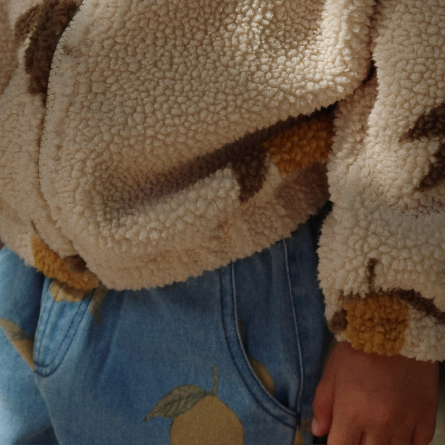 Close-up of Konges Sløjd Magot Pants in Lemon Denim and Jody Teddy Jacket – A cosy-textured teddy fleece meets soft blue denim adorned with delicate lemon prints. Thoughtfully designed for little explorers who love comfort with a touch of playful charm.