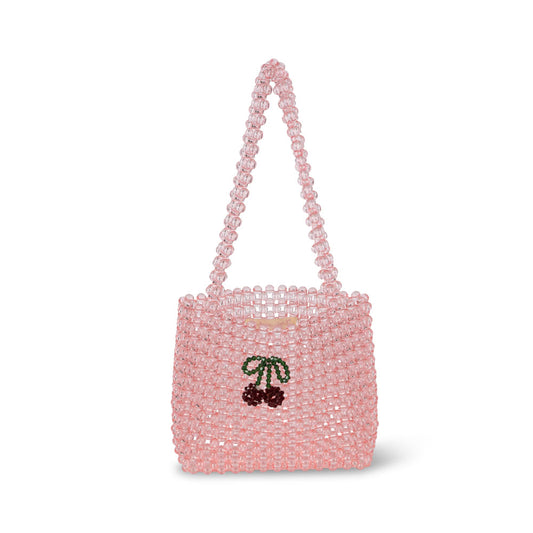 A small pink beaded handbag by Konges Sløjd. This structured tote-style bag is crafted from translucent pink beads and features a short beaded handle. A charming cherry motif, made from red and green beads, is embroidered on the front. The open-top design provides easy access to small essentials, making it a playful and stylish accessory.