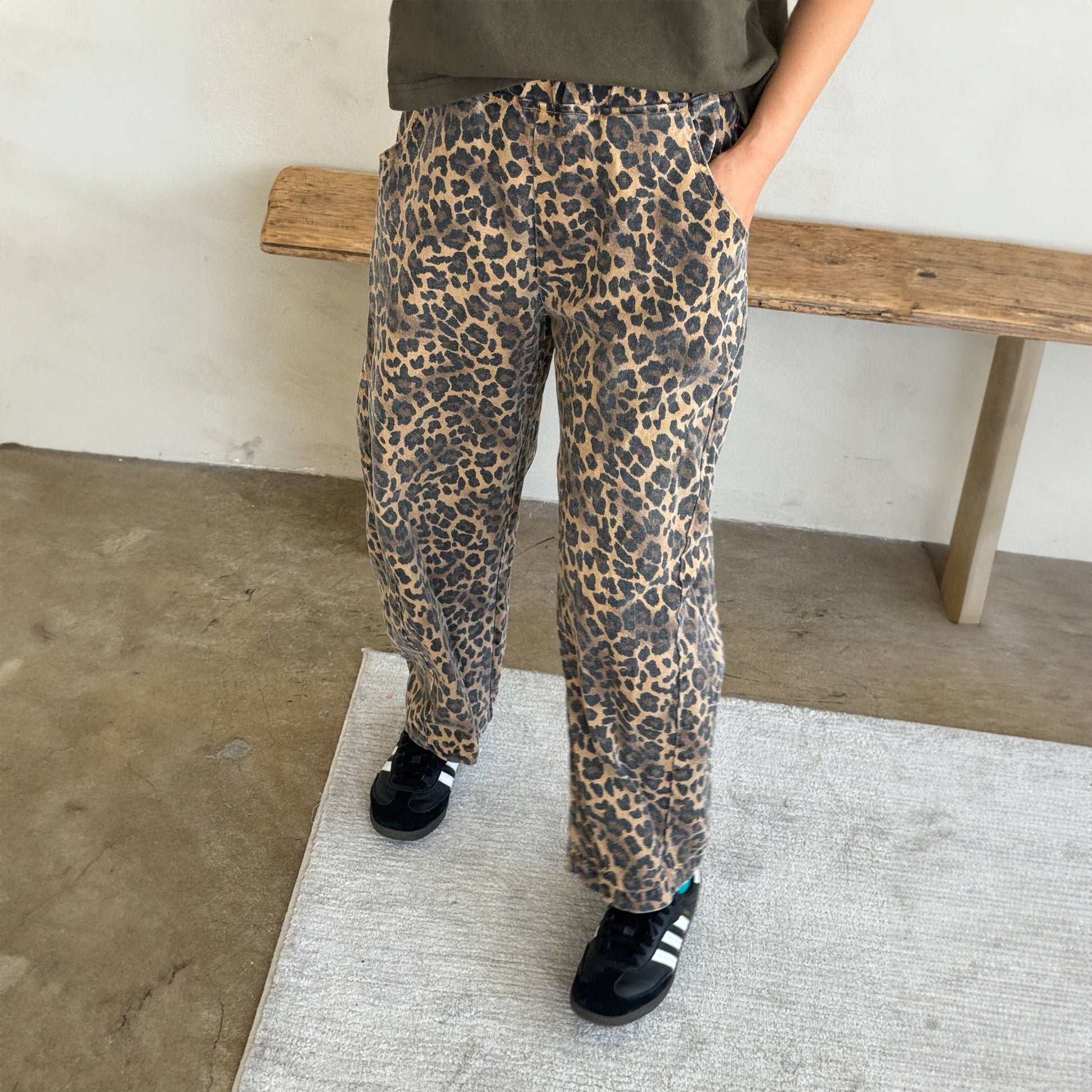 Model wearing the Le Bon Shoppe Leopard Arc Pants, cropped at the ankle with a relaxed fit and elasticated waist, styled casually with black trainers and a khaki tee.