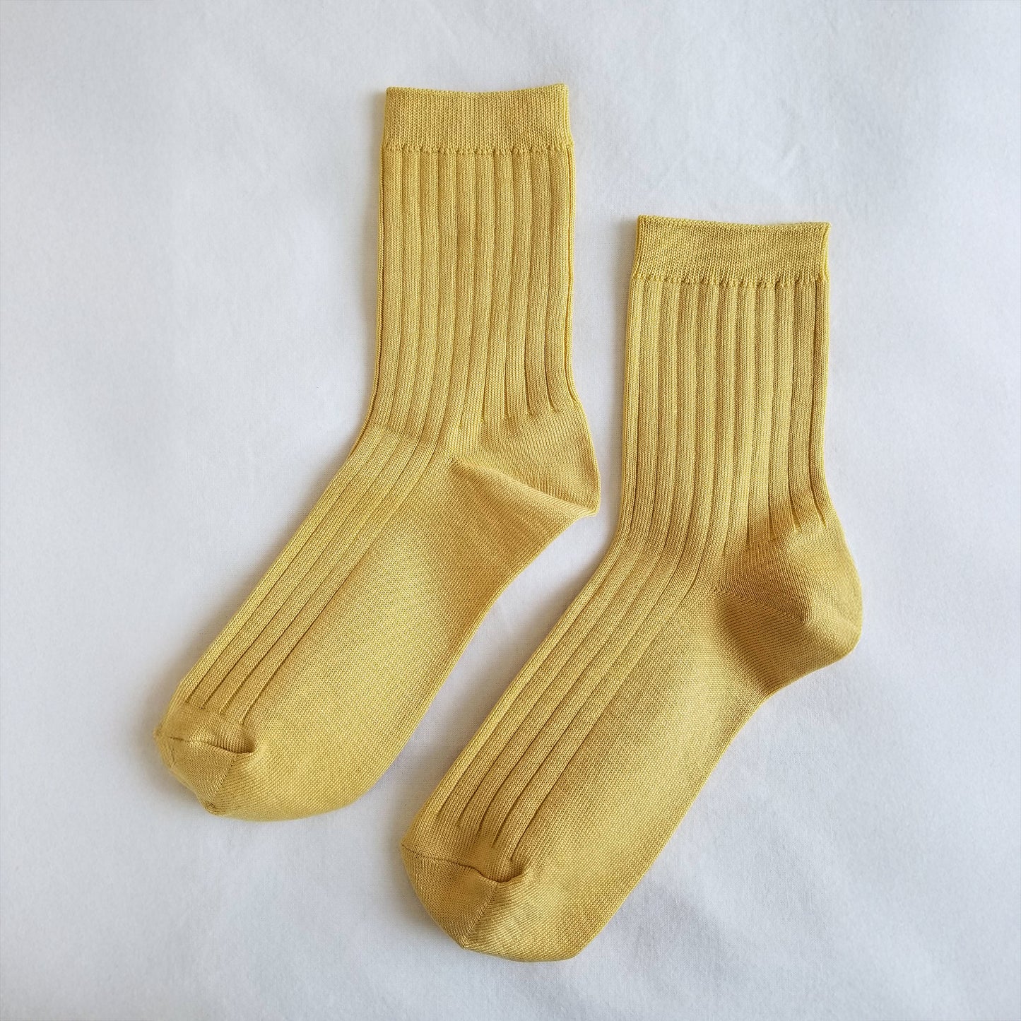 A pair of buttercup yellow ribbed crew socks laid flat on a soft white fabric background.