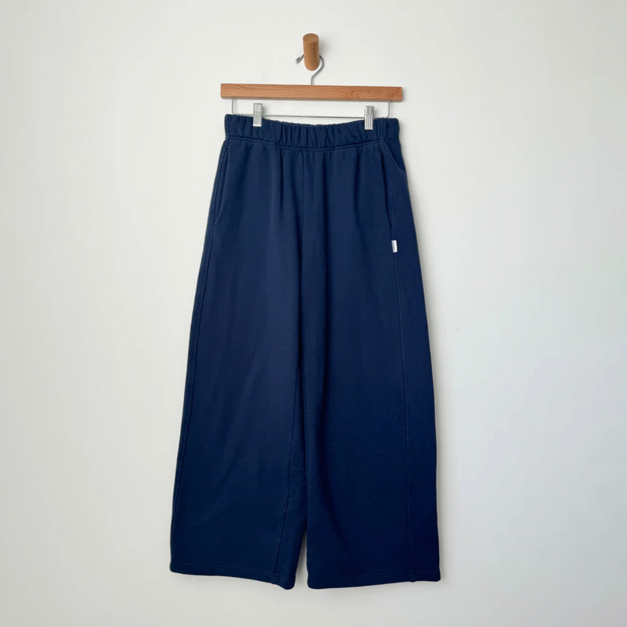 Le Bon Shoppe Breezy Pants in Midnight Blue, made from soft cotton French Terry, featuring a wide-leg design with an elasticated waistband and side pockets, hanging on a wooden hanger against a white background.