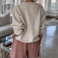 Person wearing a naturel sweater and pink pants in a room with a couch and windows.