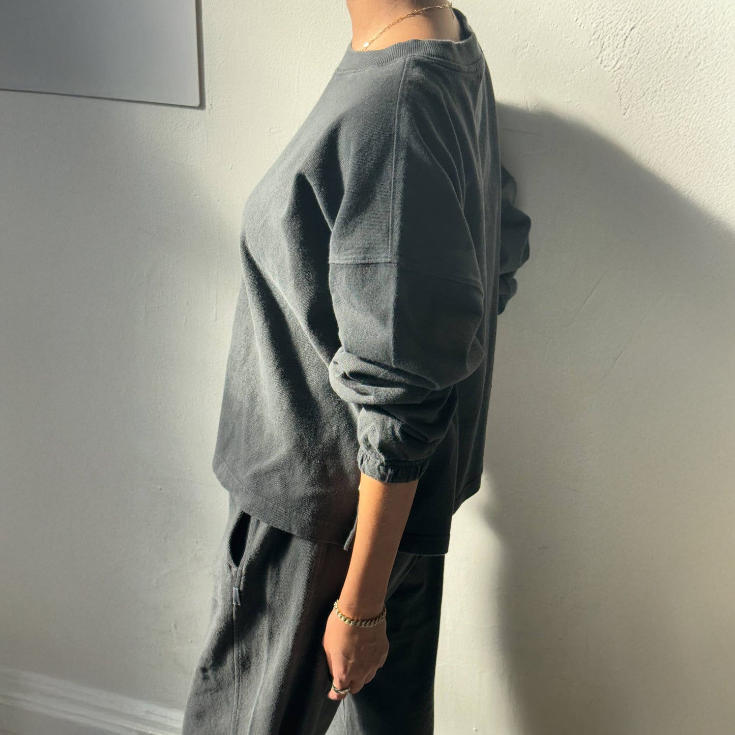 Side view of the Le Bon Shoppe Naturelle Tee in Coal – A casual long-sleeve tee with an oversized fit, subtle balloon sleeves, and garment-dyed texture, styled with light trousers.