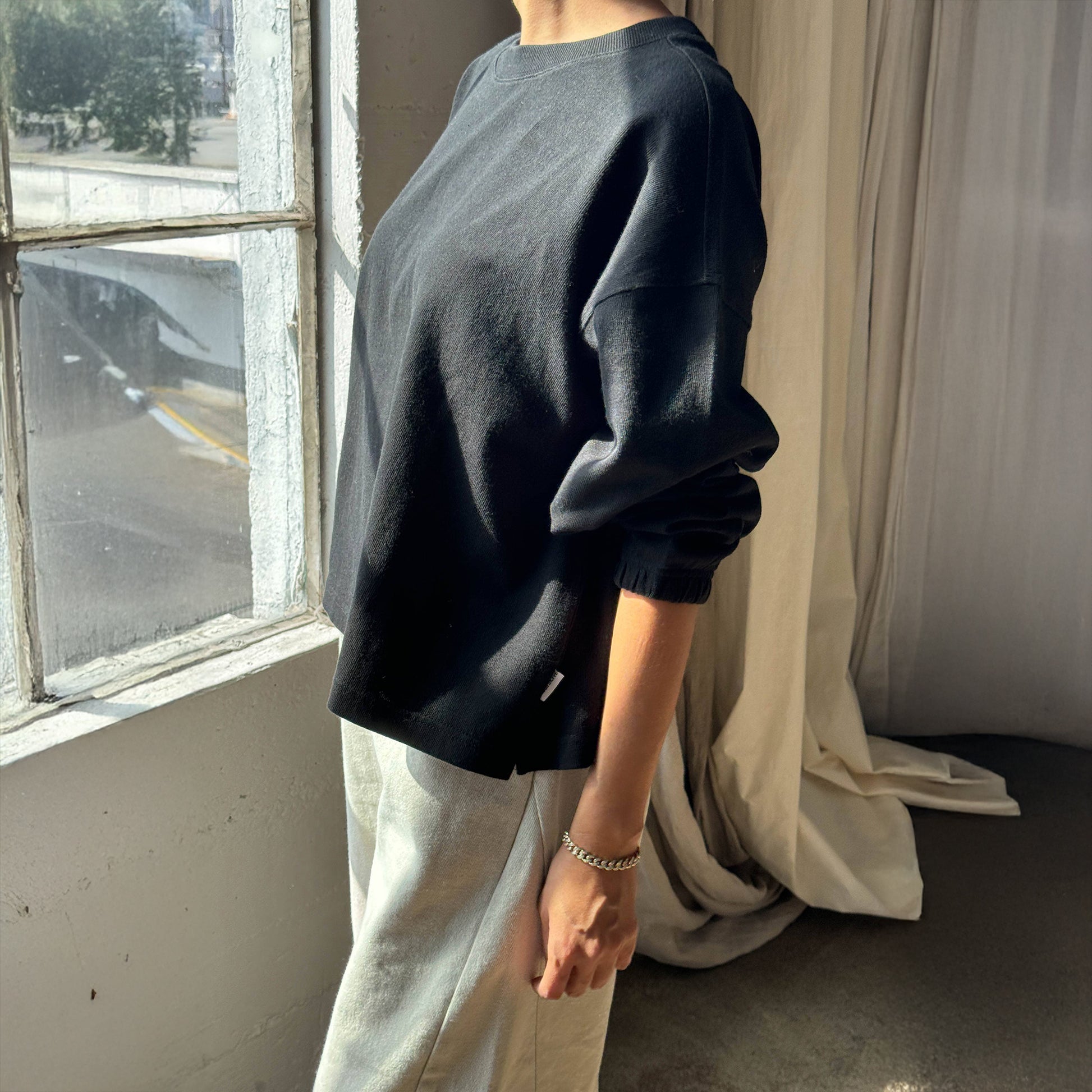 Side profile of the Le Bon Shoppe Naturelle Tee in Coal – The relaxed silhouette, ribbed neckline, and textured heavyweight cotton fabric are accentuated in natural sunlight.