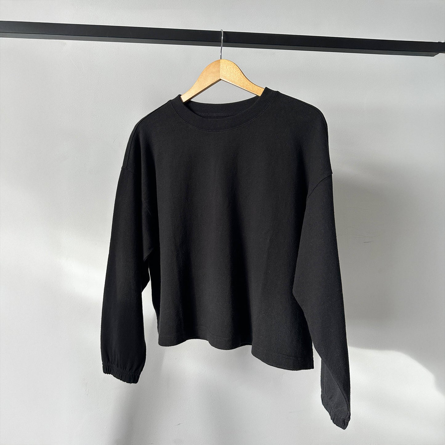 Le Bon Shoppe Naturelle Tee in Coal hanging on a wooden hanger – The tee is displayed at an angle on a clothing rail, highlighting its minimal design, soft fabric, and garment-dyed finish.