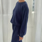 Person wearing a navy blue sweatshirt and pants in a minimalistic room with white curtains.