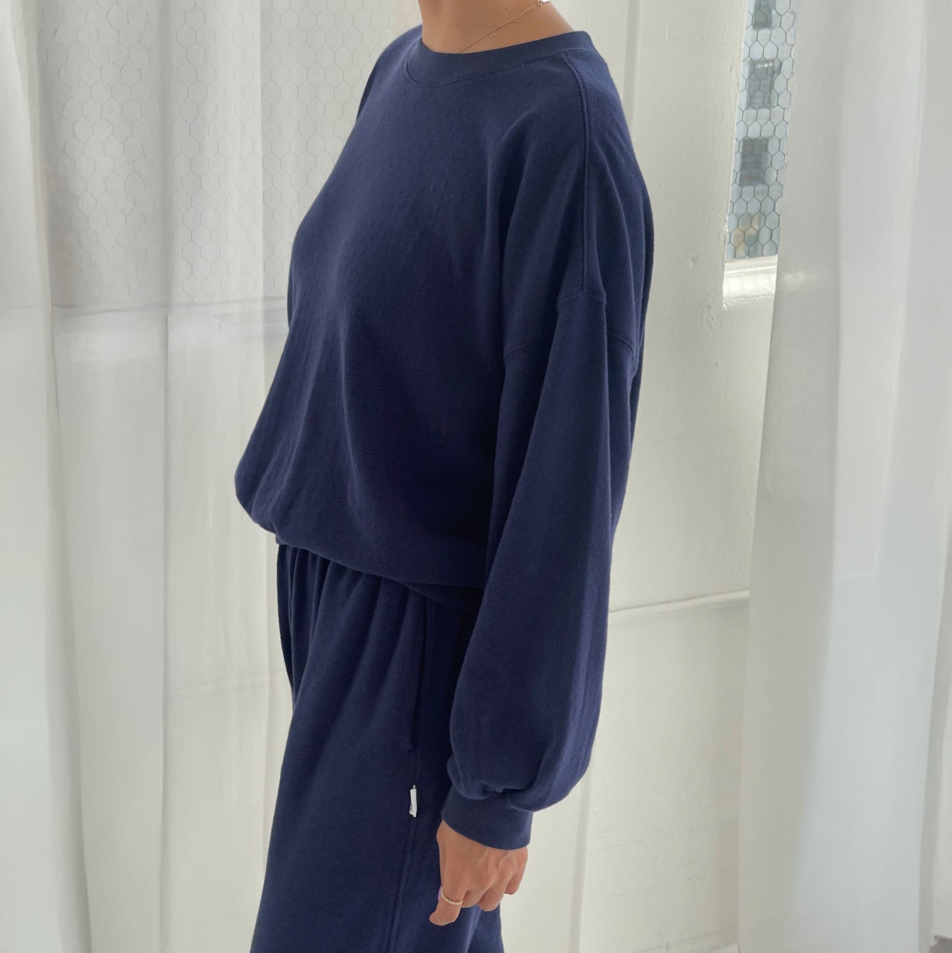 Person wearing a navy blue sweatshirt and pants in a minimalistic room with white curtains.