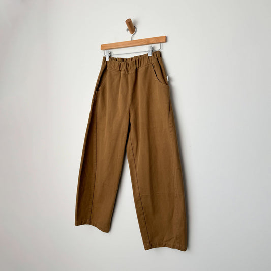 a brown tan pair of denim balloon style curved pants with an elasticated waist band and side pockets. there is a curved seam down the sides of the trouser legs