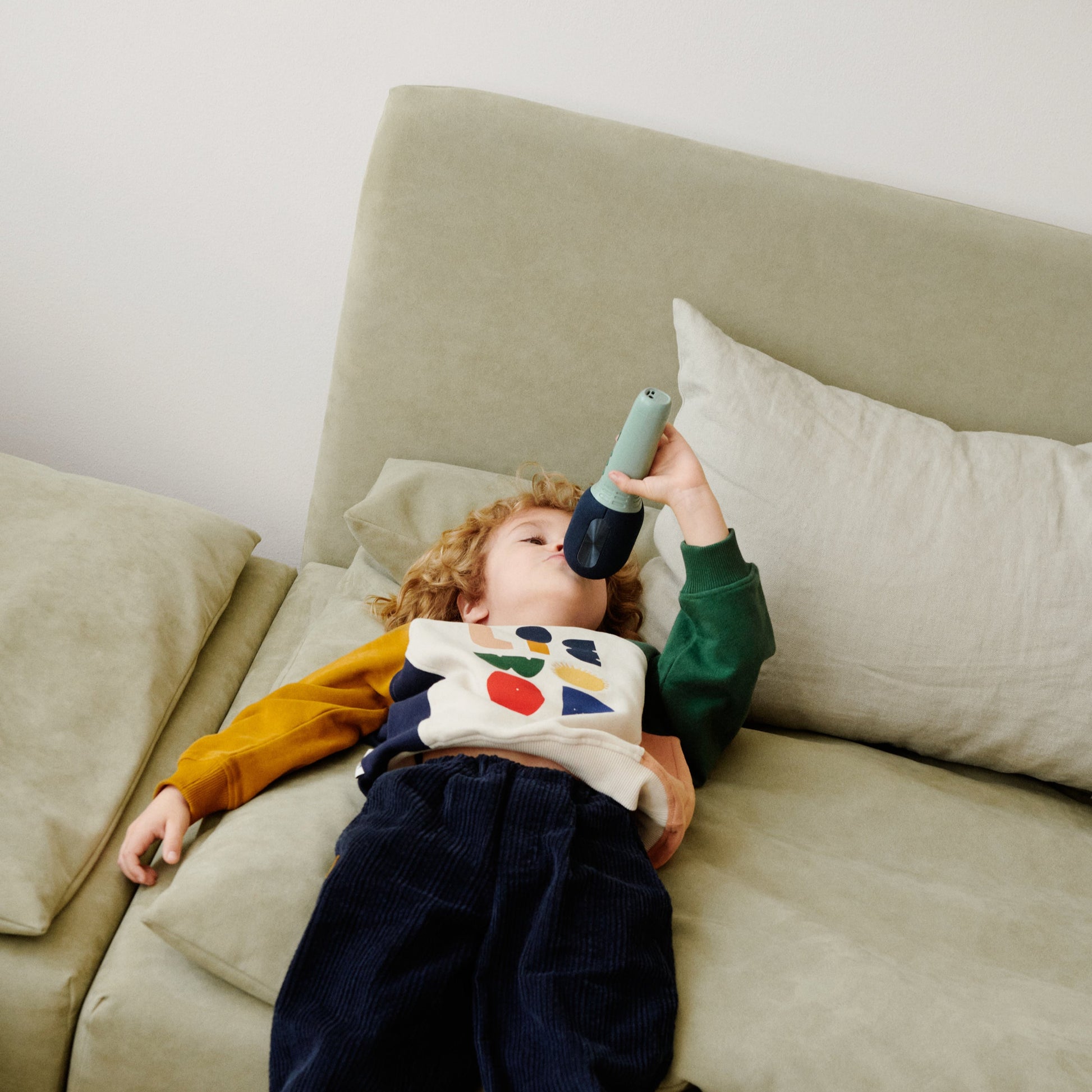 Child lying on a couch holding a toy microphone