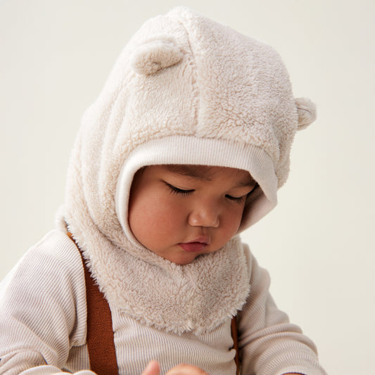 Child wearing a cream balaclava with bear ears on a plain background