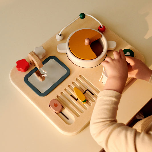 Child playing with a wooden kitchen toy set on a beige table