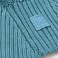 Close-up of a teal knitted balaclava with a logo patch.