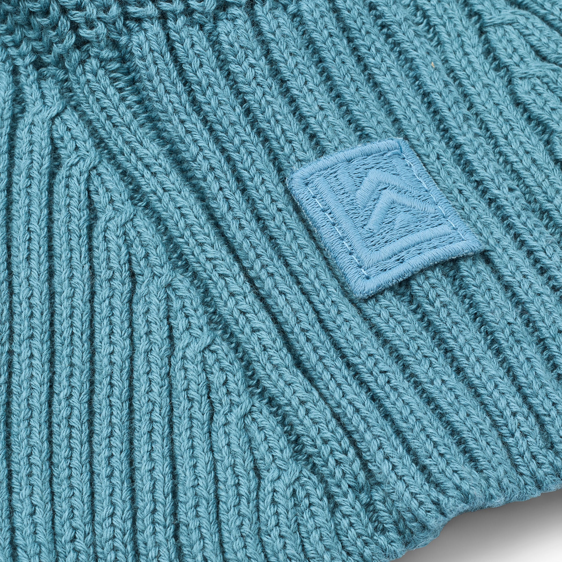 Close-up of a teal knitted balaclava with a logo patch.