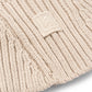 Close-up of a beige knit beanie with a brand logo on a light gray background
