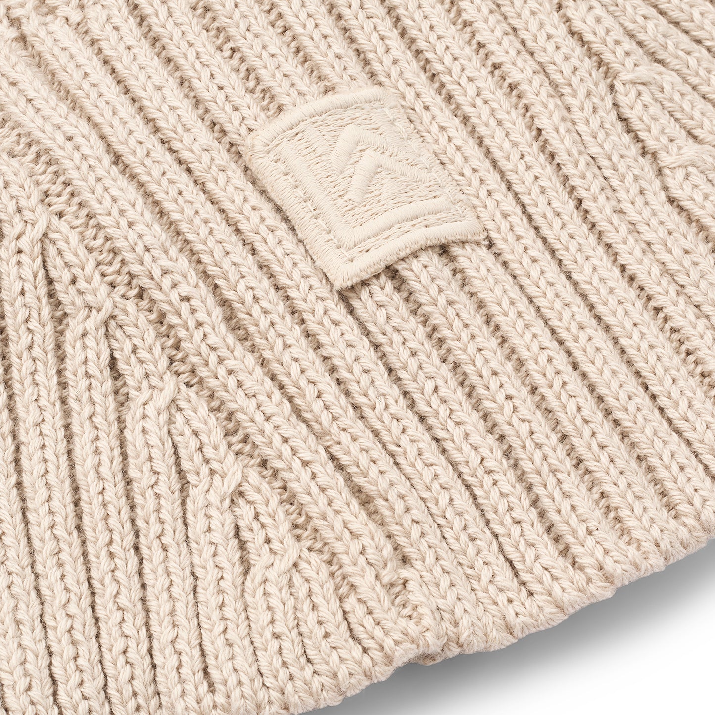 Close-up of a beige knit beanie with a brand logo on a light gray background