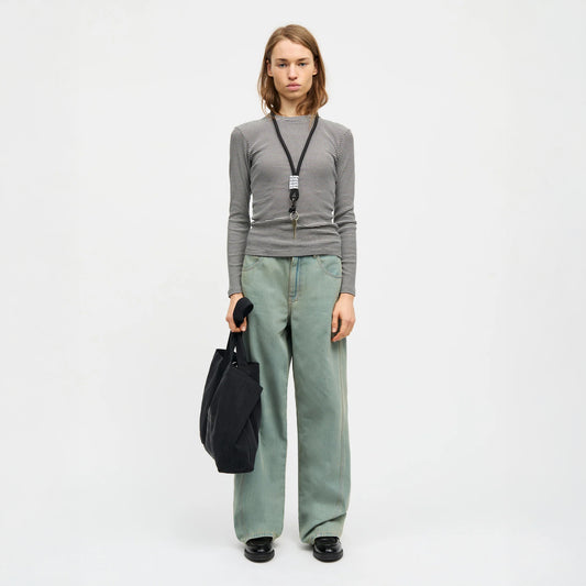 Person wearing a grey long-sleeve shirt and light blue jeans, holding a black bag on a white background
