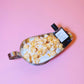 Popcorn in a metal bowl with a bottle of perfume on a pink background