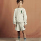 Child wearing a light gray sweatshirt and shorts set with a brown background