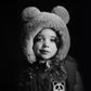 Black and white photo of a child wearing a fluffy bear hat with a dark background