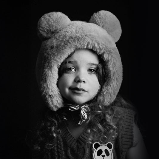 Black and white photo of a child wearing a fluffy bear hat with a dark background