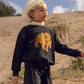 Child wearing a black sweatshirt with a mammoth design in a desert setting