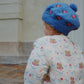 Child wearing a blue knitted hat with floral patterns, standing outdoors.