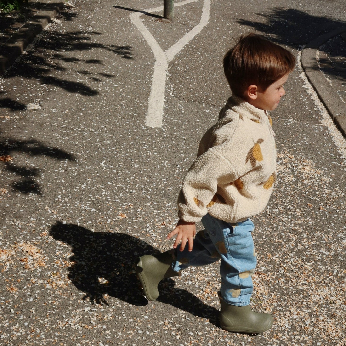 Child wearing Konges Sløjd Magot Pants in Lemon Denim and Jody Teddy Jacket – A little adventurer on the move in soft blue denim covered in playful lemons, layered with a snug teddy fleece and sturdy wellies. A perfect mix of cosy and cool.