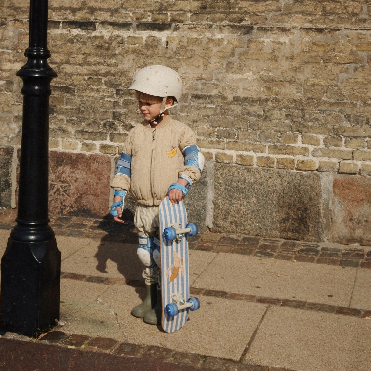 Child holding a skateboard against a brick wall