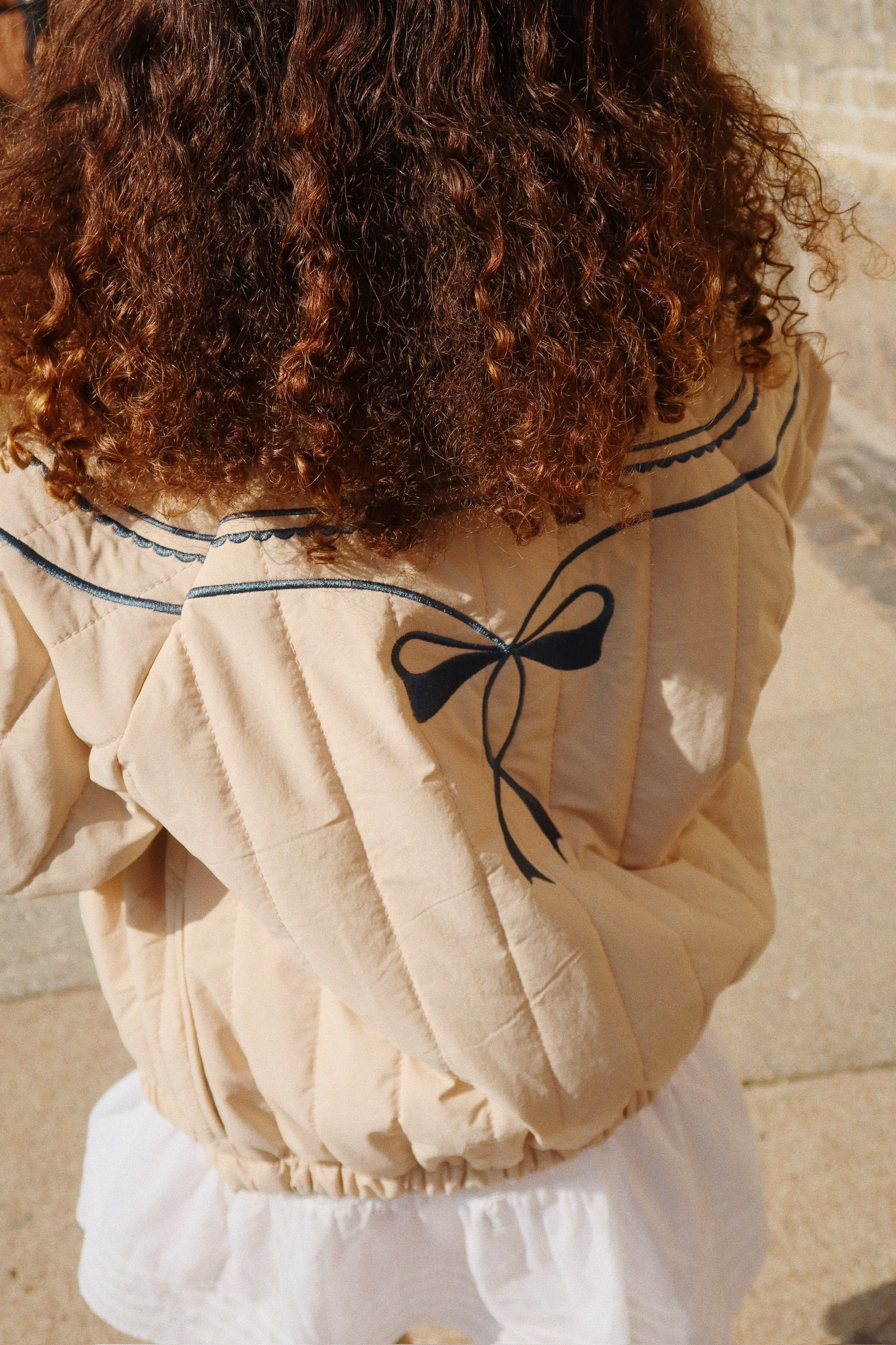 Beige puffer jacket with a black bow detail on a neutral background