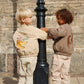 Two children in coordinated outfits standing next to a black lamp post against a stone wall.