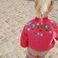 Child wearing a pink jacket with floral embroidery on a cobblestone street