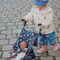 Child pushing a floral stroller with a doll on a cobblestone street