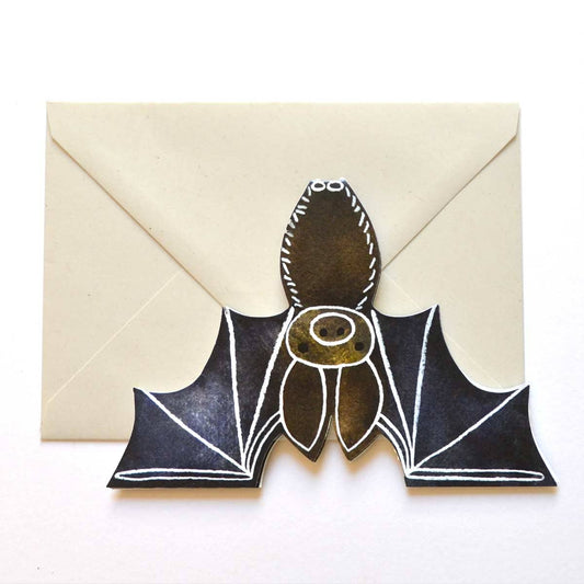 A greeting card die cut in the shape of a bat upside down, against a cream coloured envelope