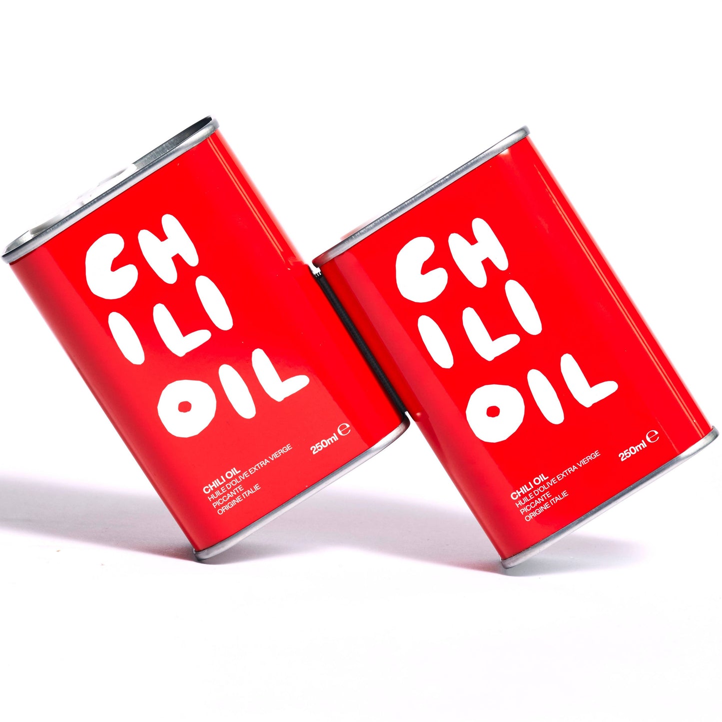 Two Olea Pia red tins of chilli oil are leaning to their left against each other. They sit on a write background and cast a shadow 