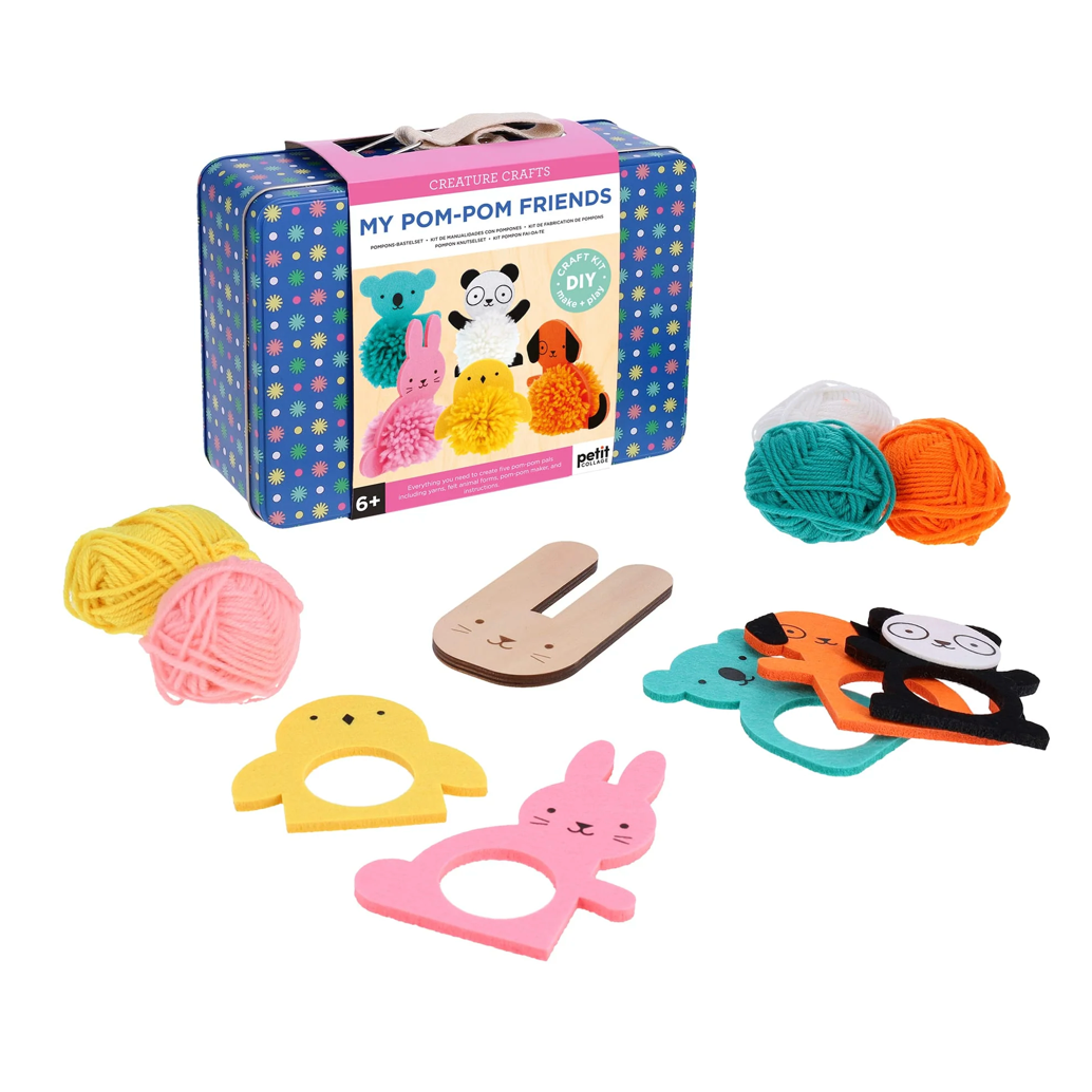 A blue tin case with a cotton handle, featuring a cardboard wrap showing the finished pom pom creatures. Lying outside the tin are five coloured balls of wool in yellow, pink, teal, white, and orange, alongside matching coloured foam shapes in the shape of animals (chick, rabbit, koala, dog, panda), and a wooden bunny shaped pom pom maker.