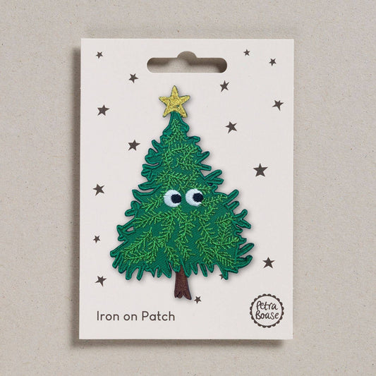  an embroidered Christmas tree with a golden star on top. It has black eyes with light and dark green leaves. The bark is brown in colour. The background is white with black stars