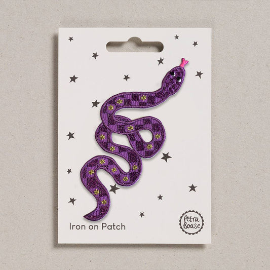 An embroidered purple snake with pink tongue. It has black eyes. Its body is adorned with light and dark purple checks and golden stars. The background is white with black stars 