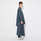 Side view of the model wearing the oversized blue checkered shirt and skirt, showing the long, loose fit and drape of the fabric. The shirt extends past the hips with a curved hem.
