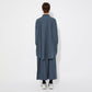 Back view of the model wearing the oversized blue checkered shirt and skirt, displaying the relaxed fit and drape. The shirt features a straight yoke and a slight pleat at the back for extra movement.