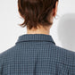 Close-up of the back collar of the blue checkered shirt, showing the soft cotton fabric and subtle grid pattern. The stitching and texture of the material are visible.