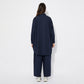Back view of the model in the navy oversized cotton shirt, showing its extended drape, back yoke detail, and soft folds in the fabric. The loose fit allows for movement while maintaining structure.