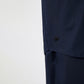 Close-up of the lower part of the navy oversized cotton shirt, focusing on a small, subtly embroidered black logo near the side seam. The fabric has a smooth, matte finish, and the hem is slightly curved.