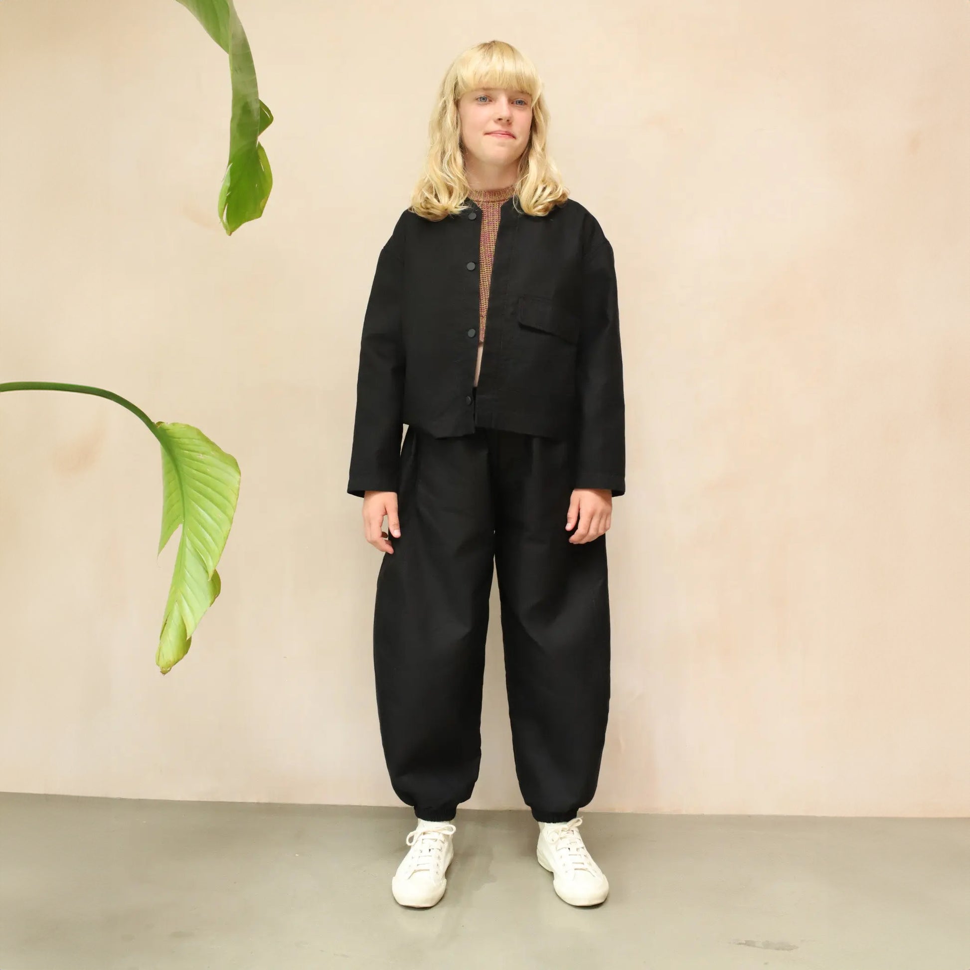 A pair of Otis Woven Wide-Leg Trousers in versatile black, showcasing a relaxed rounded silhouette, gathered cuffs, and an elastic waistband with an internal drawcord. The trousers are made from soft, washed double cotton and feature pockets for added practicality. The blonde haired model wears with a striped roll necked top and matching black jacket