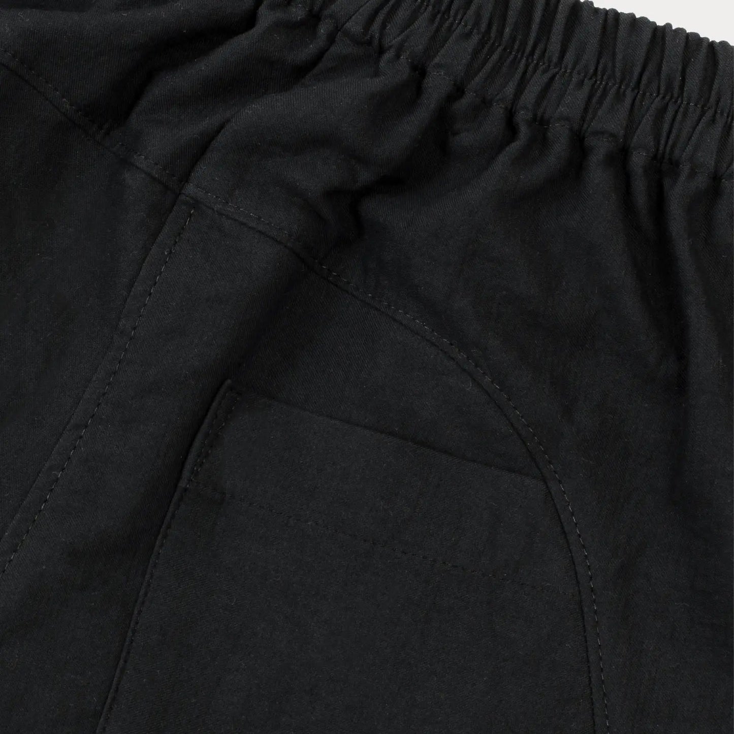 A close up of a pair of Otis Woven Wide-Leg Trousers in versatile black, showcasing a relaxed rounded silhouette, gathered cuffs, and an elastic waistband with an internal drawcord. The trousers are made from soft, washed double cotton and feature pockets for added practicality. 