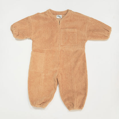 Studio Koter Rae Oversized Teddy Boilersuit in warm caramel, showcasing the soft texture of the 100% organic cotton teddy fleece. The image highlights the zip front, elasticated cuffs, and spacious patch pockets, emphasizing the cozy and functional design perfect for cooler days. 