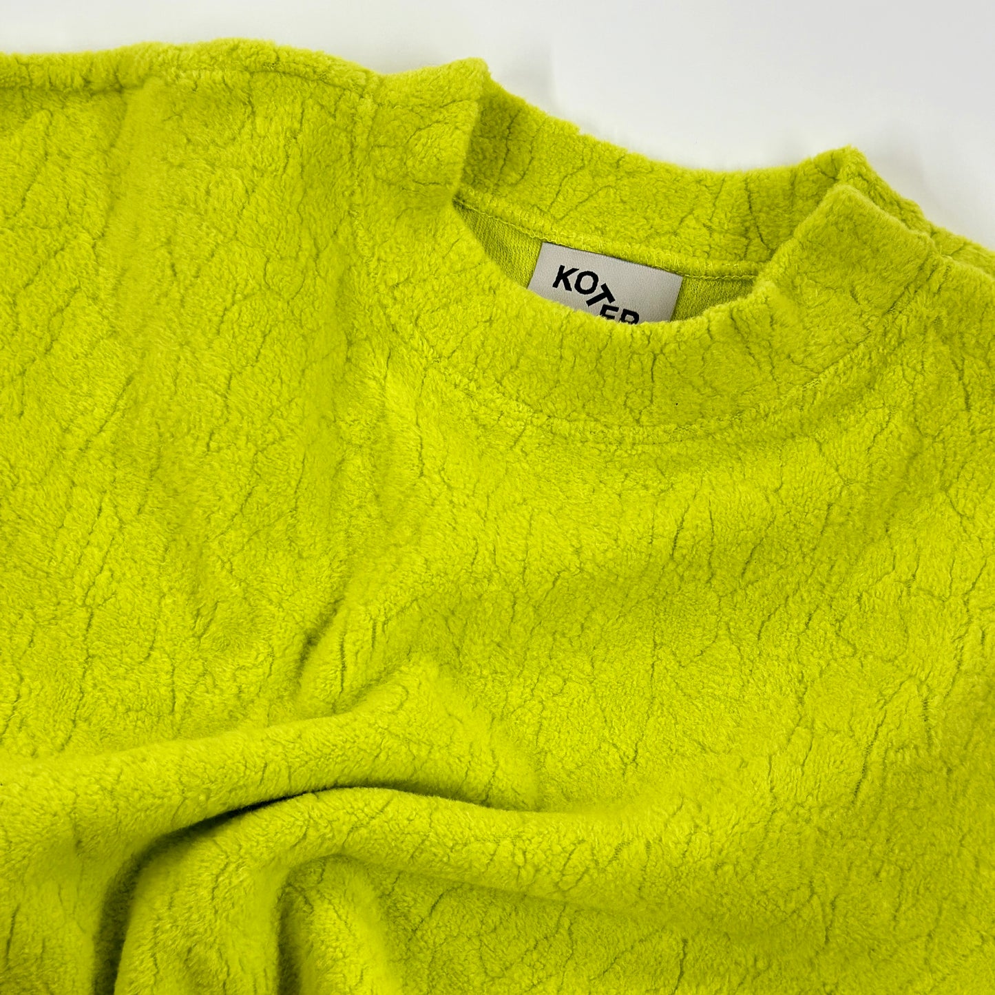 Close-up of the Studio Koter River Teddy Sweatshirt in vibrant acid green, showcasing the unique texture of the 100% organic cotton teddy fleece. The image highlights the soft, tactile quality of the fabric.